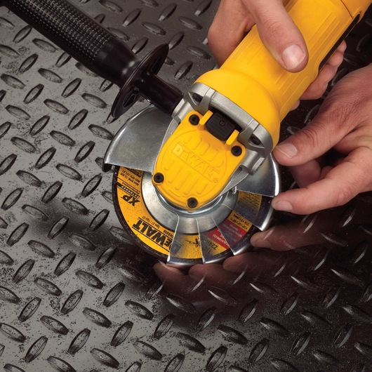 Close-up of a person using a yellow DEWALT angle grinder on a textured metal surface.