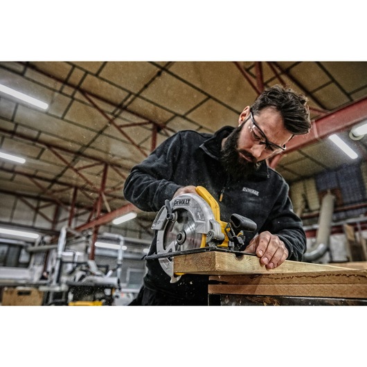 A person using a DEWALT DWE560 circular saw to cut wooden boards in a workshop, with their face blurred for privacy.