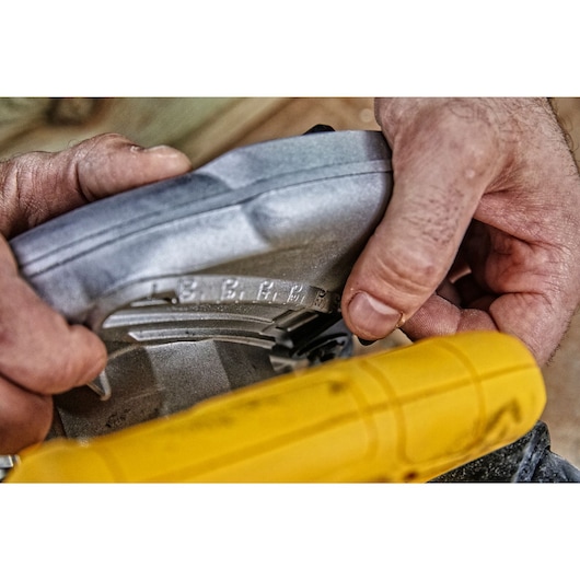 Close-up of hands adjusting the metal angle guide on a yellow DEWALT power tool, possibly a circular saw.