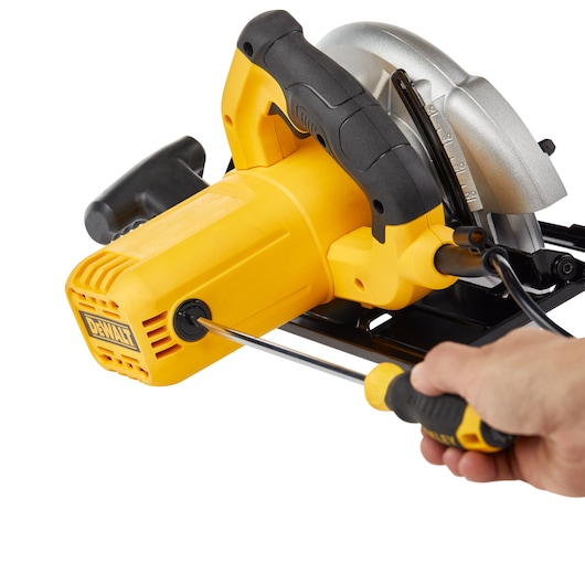 A close-up of a DEWALT yellow circular saw being serviced with a screwdriver, focusing on the motor casing and handle.