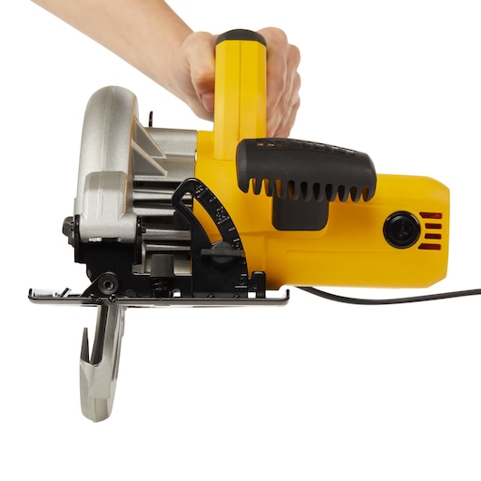 A close-up of a hand holding a DEWALT DWE5615 yellow circular saw, showing its handle, blade guard, and adjustment features against a plain white background.