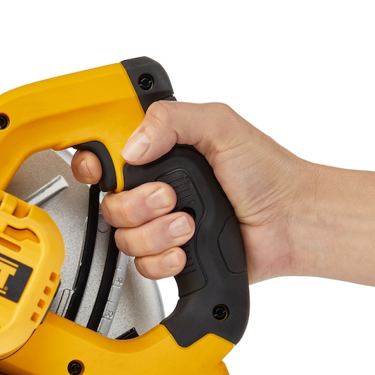 A close-up of a hand gripping the handle of a yellow and black DEWALT power tool, specifically a DWE5615 circular saw.