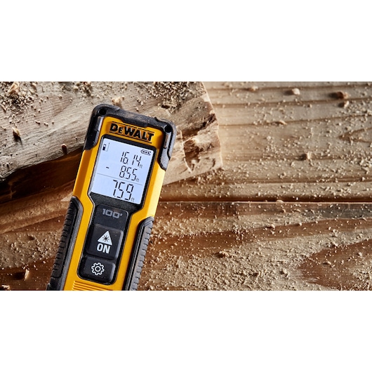 A DEWALT laser distance measurer displaying measurements on its screen, placed on a wooden surface with sawdust.