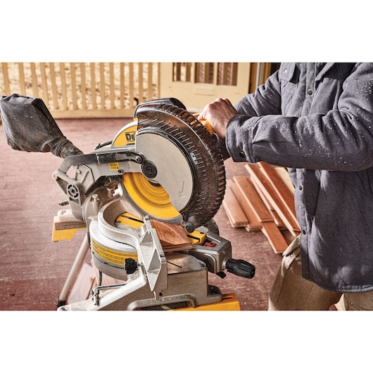 A person using a Dewalt DWS713 miter saw to cut a piece of wood, with the saw positioned on a workbench and several pieces of wood in the background.