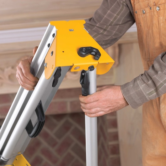 A close-up view of a person adjusting the stand of a yellow DEWALT miter saw, focusing on the legs and locking mechanism.