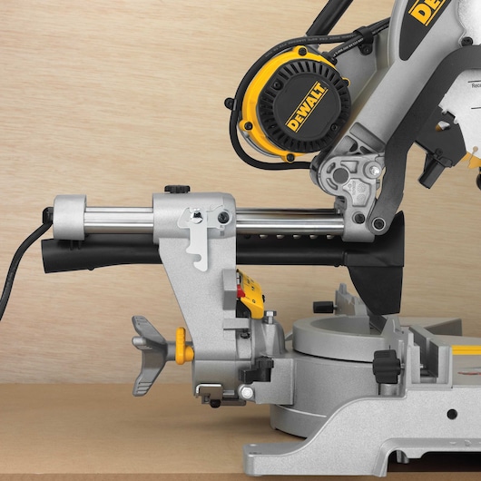 Close-up view of a DEWALT DWS780 sliding compound miter saw placed on a wooden surface, with visible power cord, motor housing, and adjustment knobs.