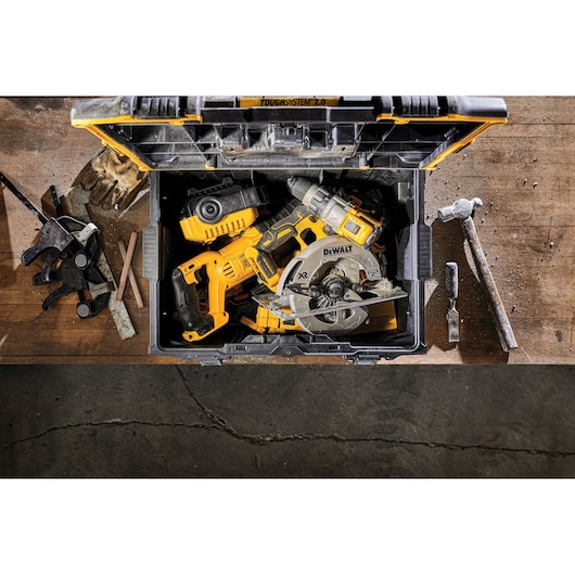 A DEWALT ToughSystem 2.0 tool box on a workbench, open to show various yellow and black power tools including a circular saw and a drill. Other hand tools and accessories are scattered around the workbench.