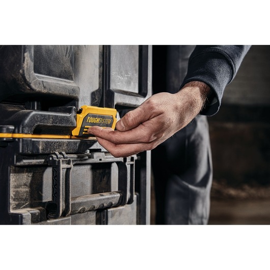 A person is operating the yellow latch mechanism on a black DEWALT ToughSystem storage box.