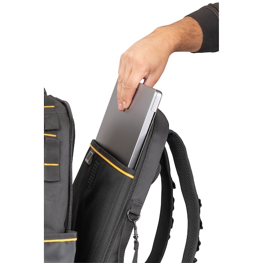 A person placing a silver laptop into the padded laptop compartment of a black and yellow DEWALT backpack.