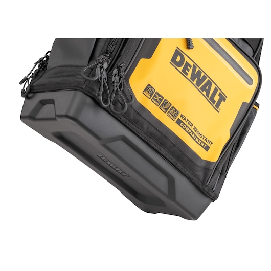 Close-up image of a DEWALT tool bag featuring a yellow and black design, with multiple zippers and a hard plastic base. The bag includes a water-resistant compartment, as indicated by the printed text and icons.
