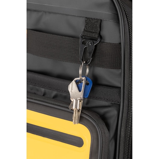 A close-up of a set of keys attached to a black strap with a metal clip on a grey and yellow bag.