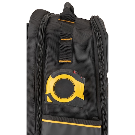 Close-up view of a black tool bag with a yellow and black measuring tape stored in an exterior pocket. The bag features a zipper and reinforced stitching.