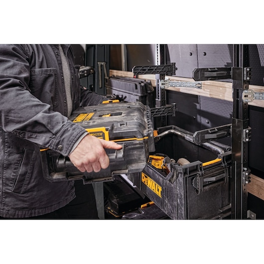 A person places a DEWALT ToughSystem toolbox onto a shelving unit or rack inside a work van or utility vehicle. The storage system is designed for organizing and transporting tools.