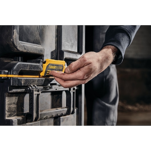Close-up of a person’s hand operating the yellow latch on a DEWALT TOUGHSYSTEM storage box.